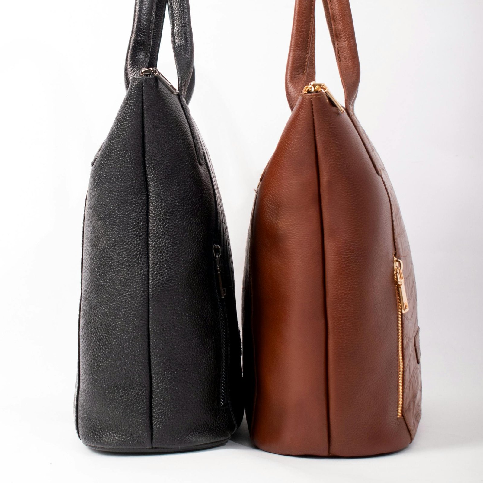 Side view of black and brown leather handbags with gold zippers on a white background.