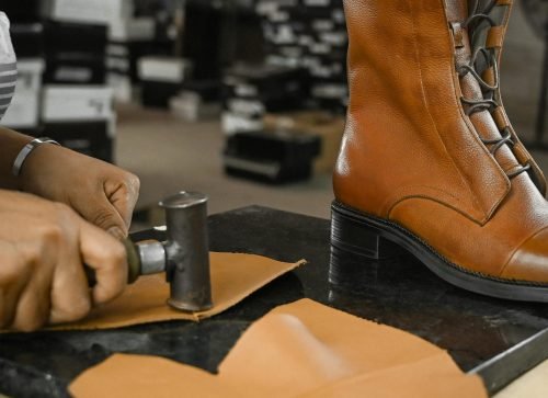 Skilled craftsman using tools to create leather boots in an industrial setting.