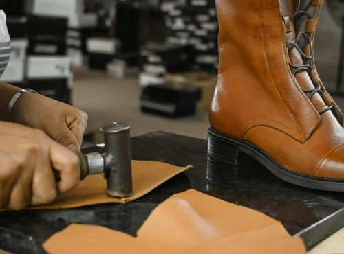 Skilled craftsman using tools to create leather boots in an industrial setting.